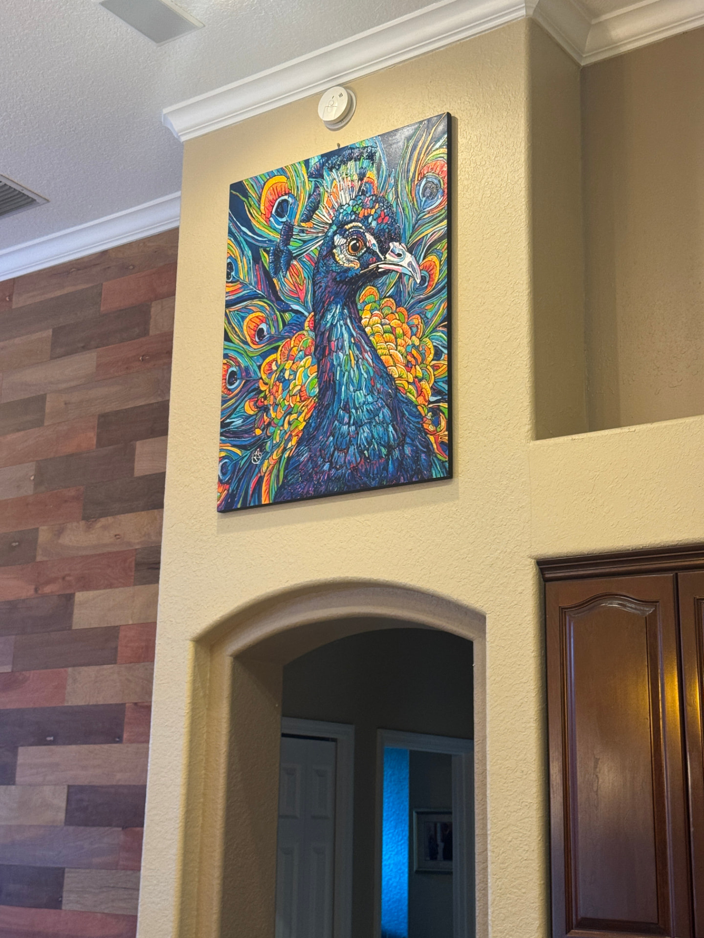 Vibrant peacock painting by Renata Rolefes hanging on a warm wall in a collector’s home