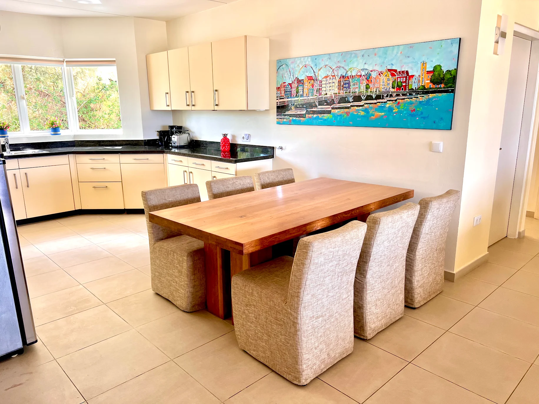 Colorful Curaçao harbor painting by Renata Rolefes above a dining table in a bright home