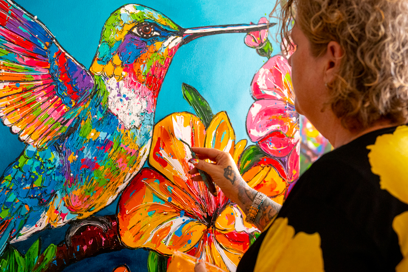Renata Rolefes painting a colorful hummingbird and hibiscus flowers in her Curaçao studio